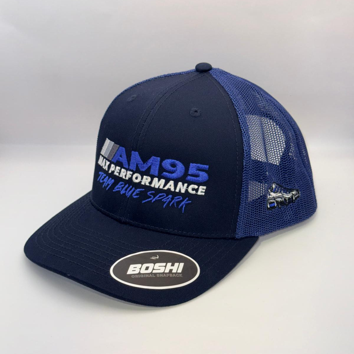 A navy blue and royal blue trucker hat with 'AM95 MAX PERFORMANCE TEAM BLUE SPARK' embroidered on the front and a 'BOSHI' sticker on the brim, set against a plain light gray background.